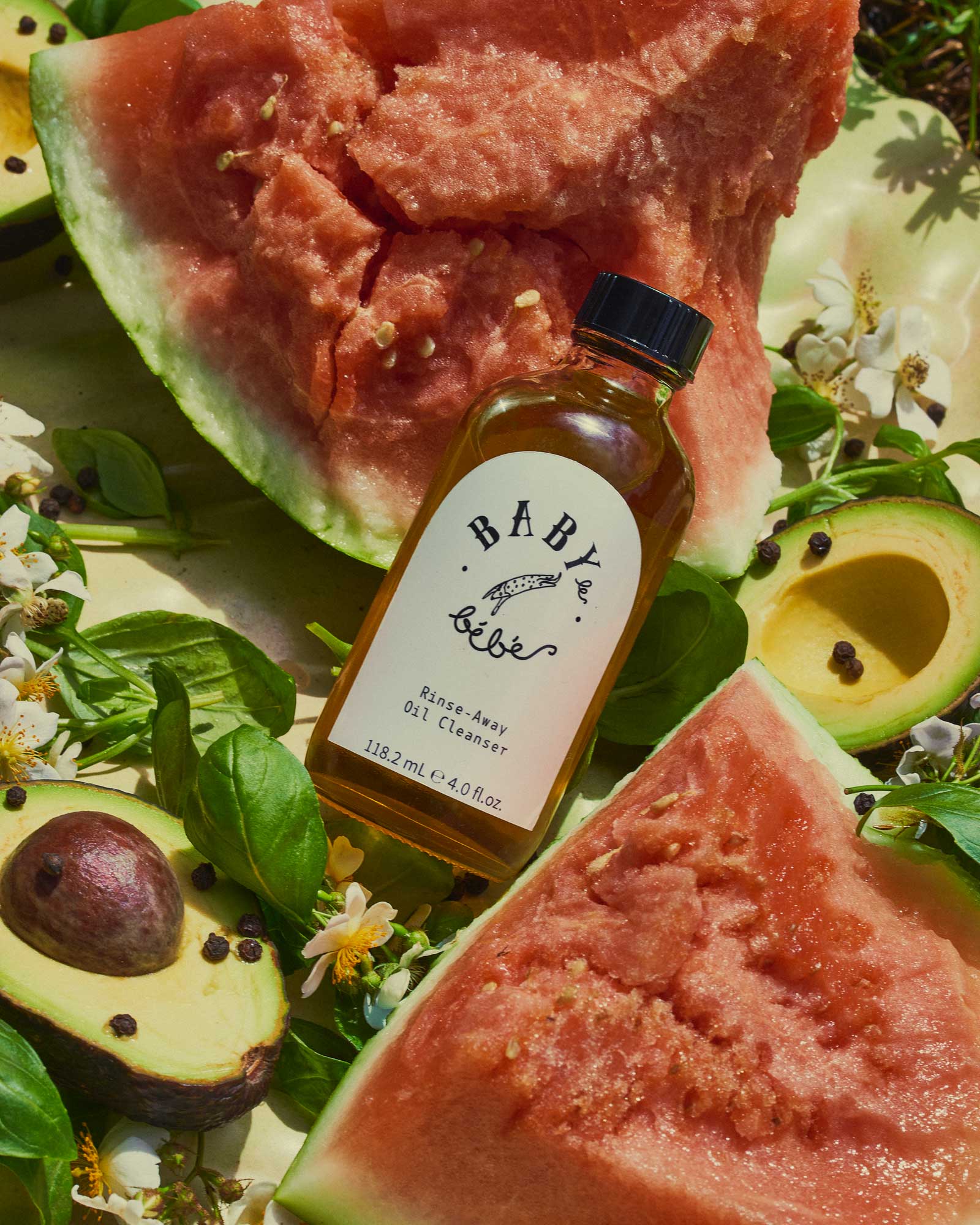 Bottle of oil cleanser lying on avocado and watermelon