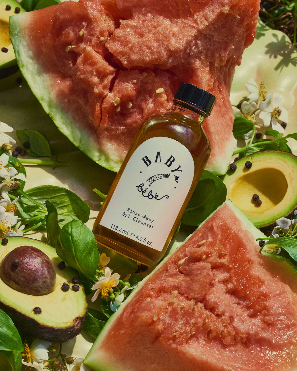 Bottle of oil cleanser lying on avocado and watermelon 