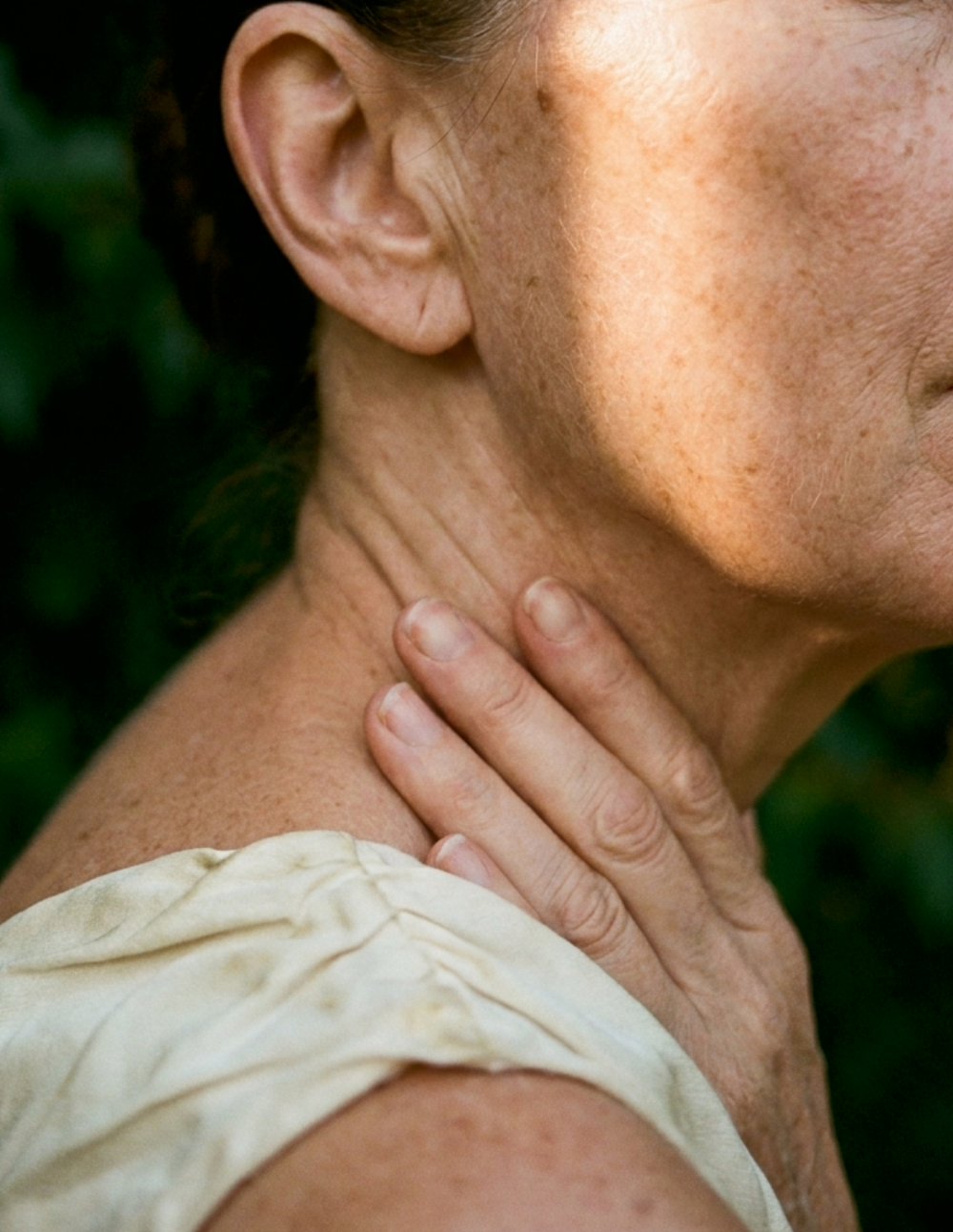 Close-up of a woman's neck and shoulder with her hand resting at her throat