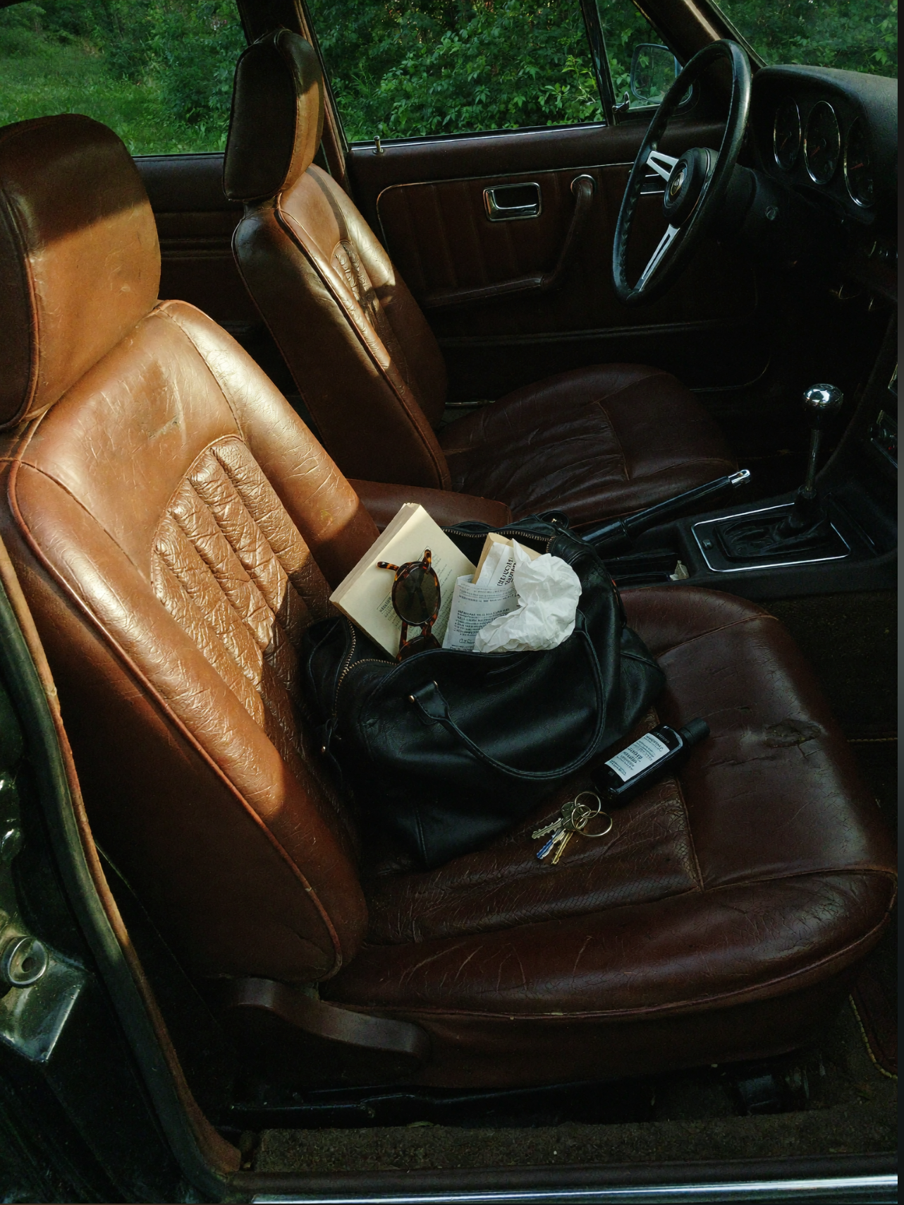 Vintage car interior with tan leather seats, a bag and keys on the passenger seat