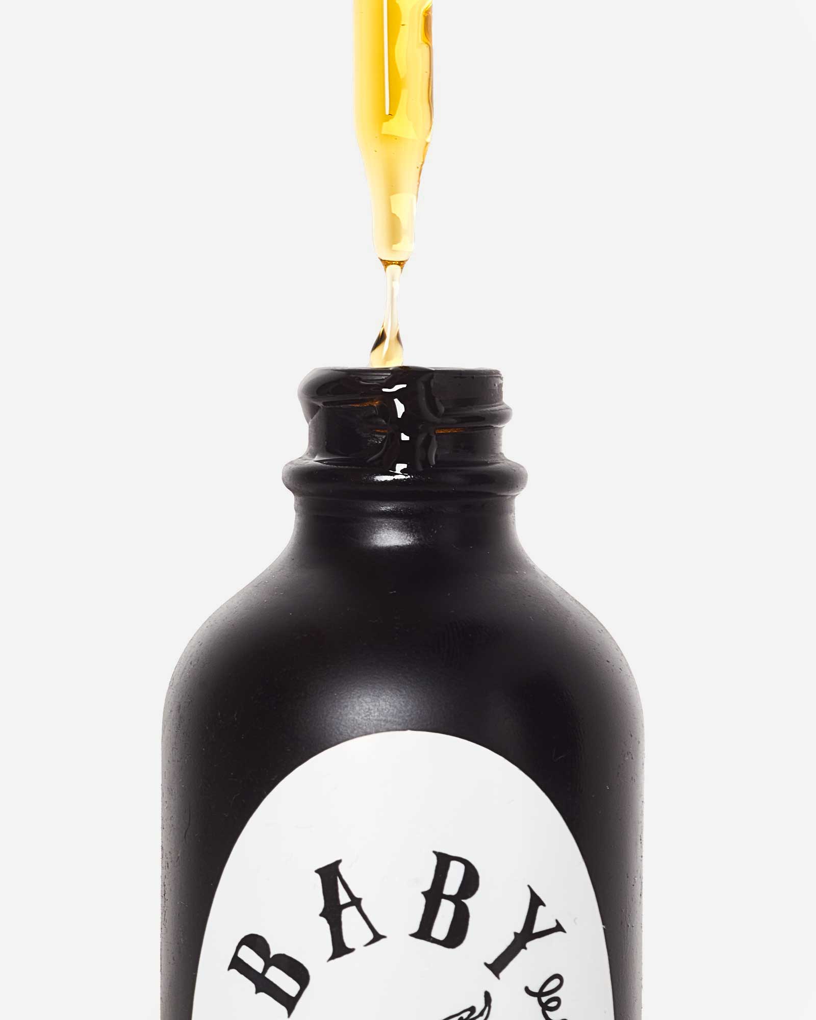 Dropper releasing golden oil above a black Baby le Bébé bottle