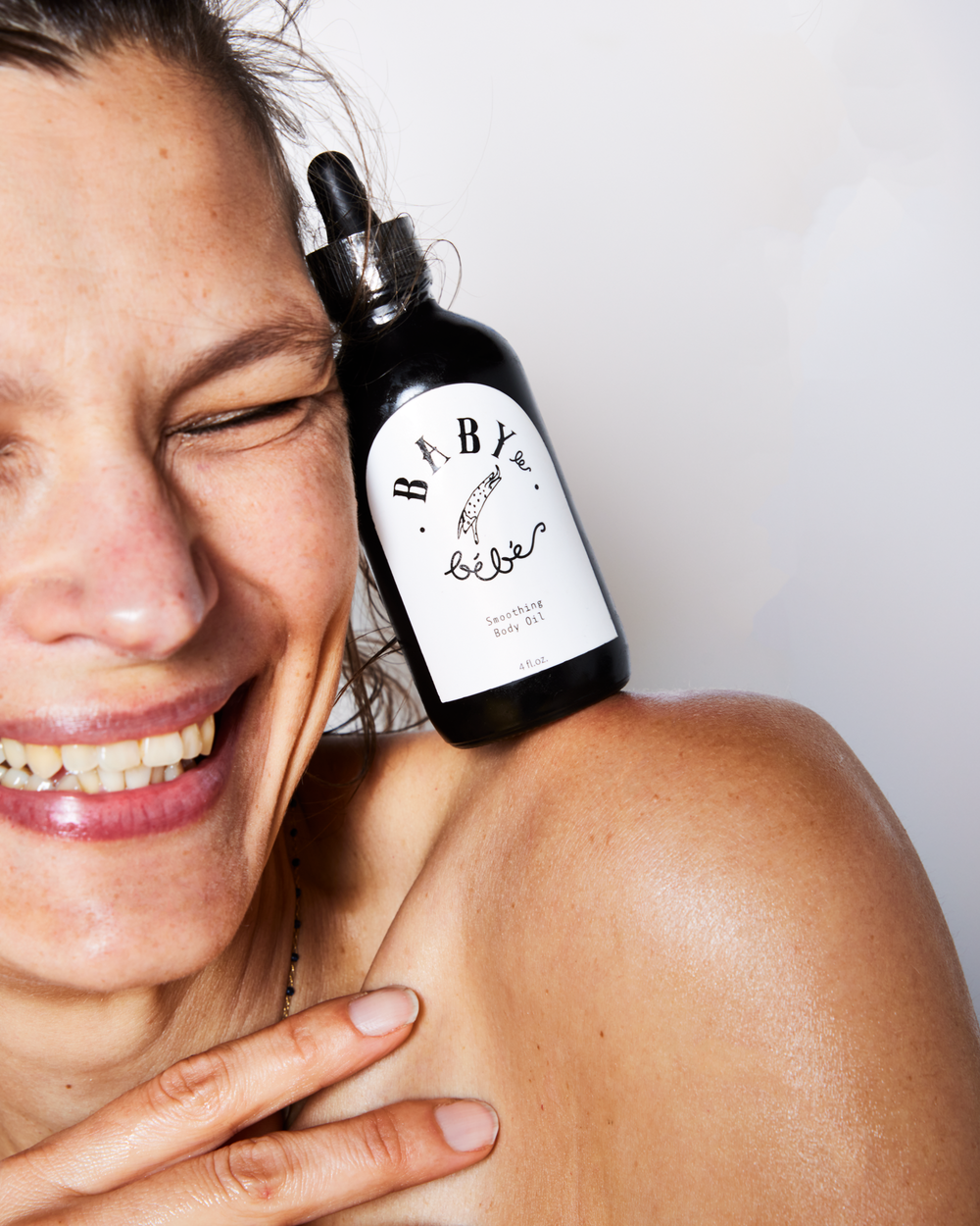 A laughing Woman balancing a bottle of face oil on her shoulder