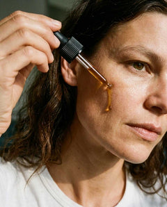 Woman applying Baby le Bébé face oil to her cheek with a glass dropper