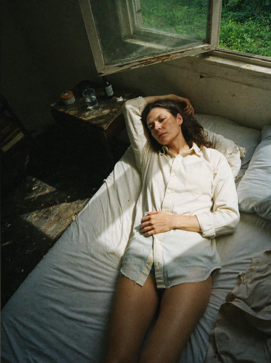 Woman in a white shirt resting on a bed beside a sunlit window