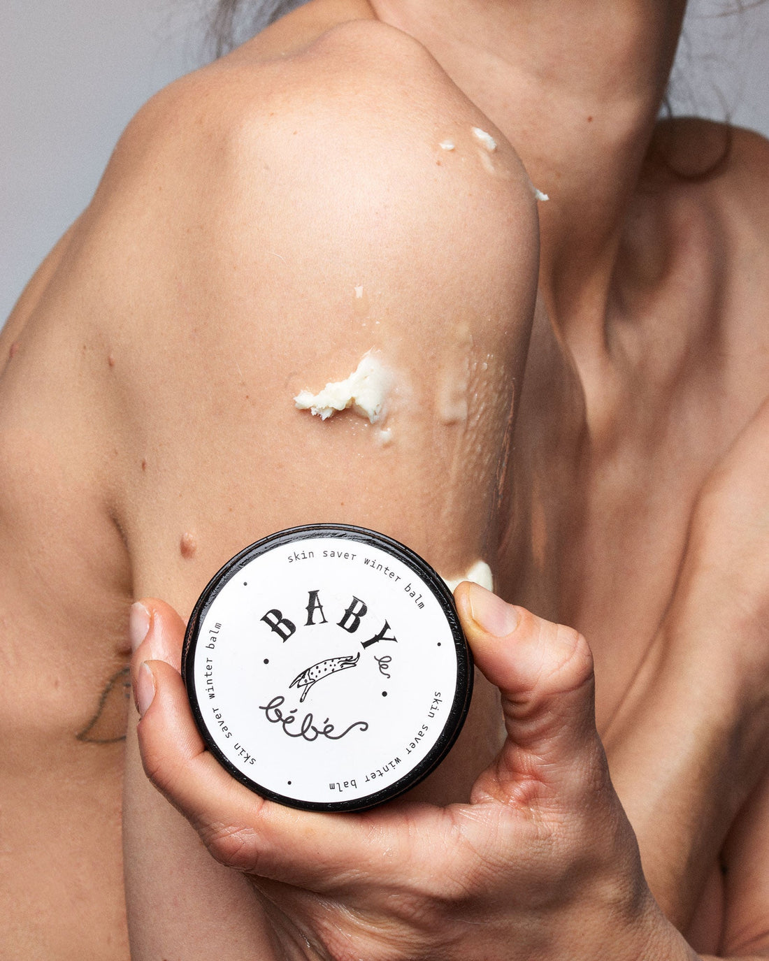 Woman showing how to apply balm to her arm and shoulder