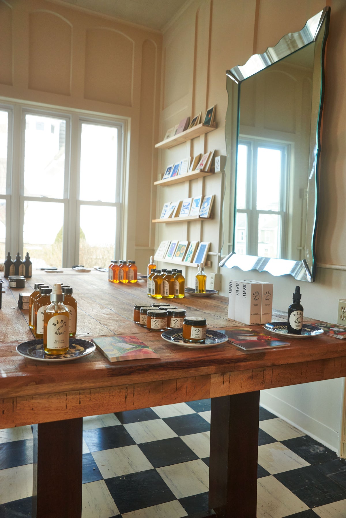 Wooden table with various bottles and jars in a room with large windows and a checkered floor.