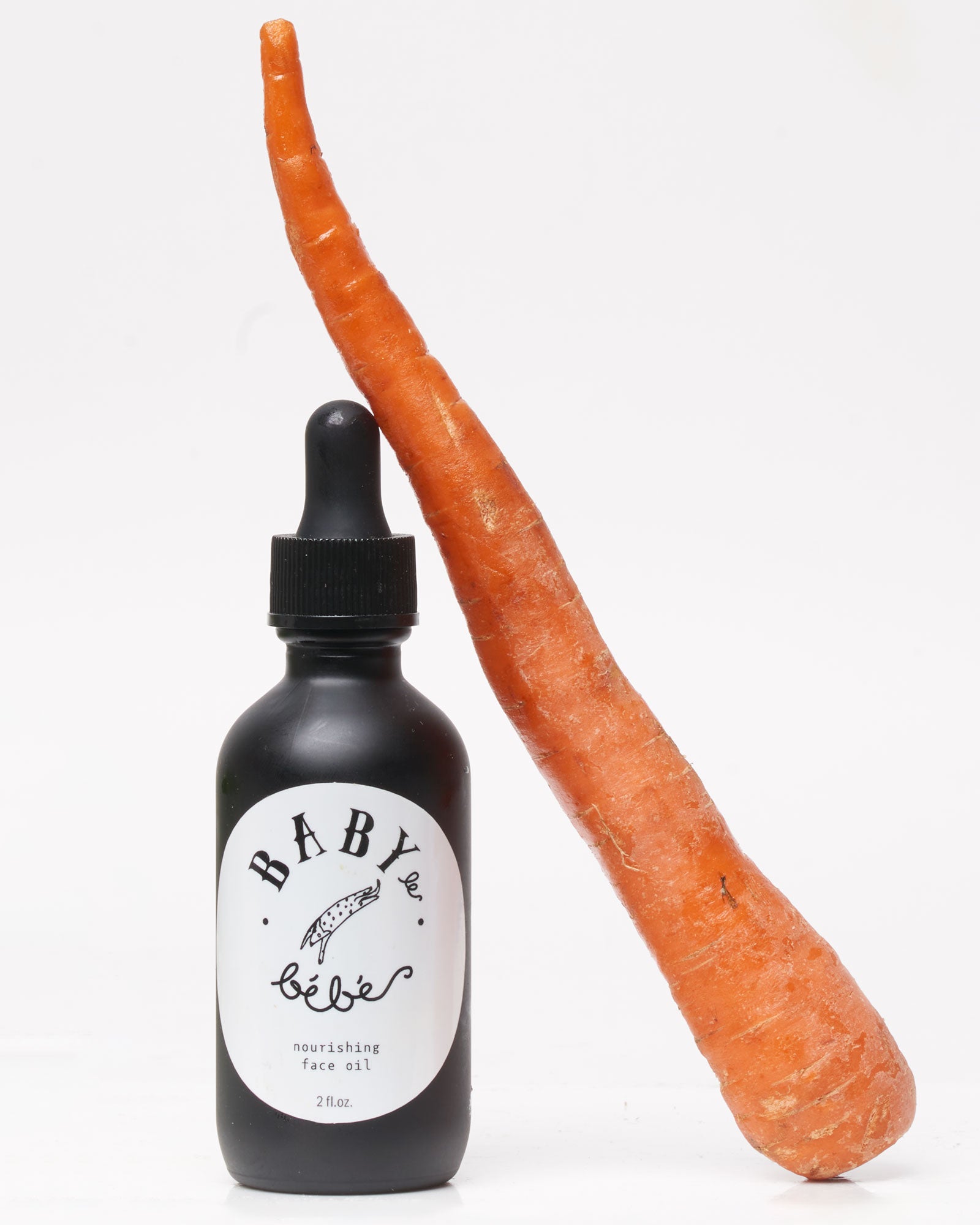 Black bottle labeled 'Baby le Bebe' with a dropper next to a carrot on a white background